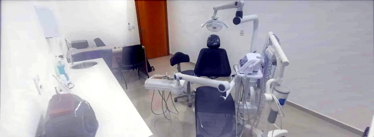 Sala de atendimento do consultório, com cadeira odontológica, refletor e bancada