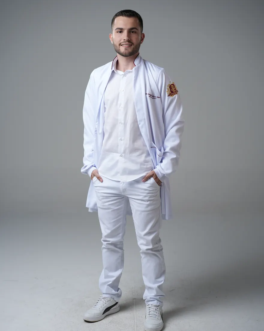 Dr. Douglas Bortoluzzo, de jaleco branco, em pé diante de um fundo de estúdio claro