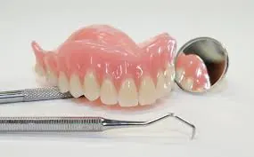 Prótese dentária total sobre bancada, ao lado de espelho e instrumentos clínicos